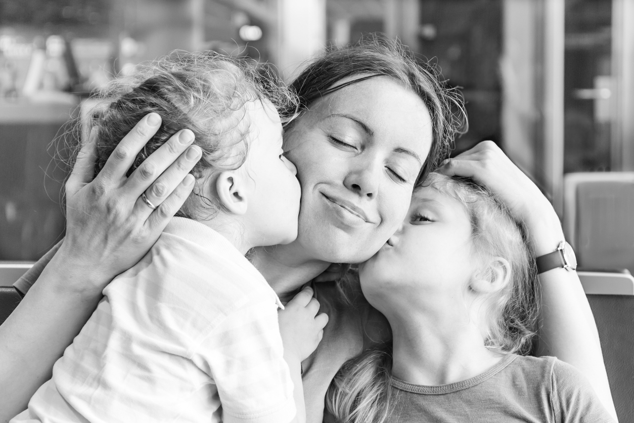 Two daughters kissing their happy mother