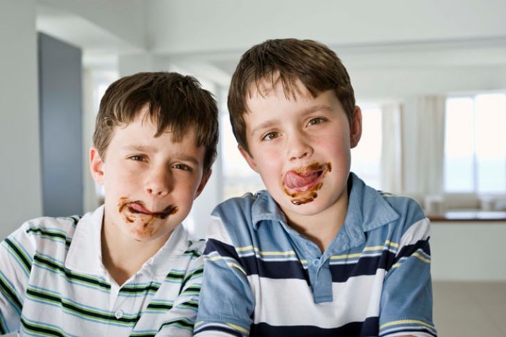 Twin boys licking chocolate on messy faces