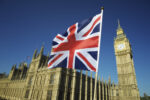 Union Jack British flag flies in bright blue sky at Houses of Parliament and Big Ben London