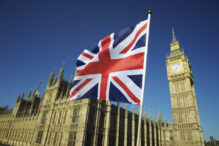 Union Jack British flag flies in bright blue sky at Houses of Parliament and Big Ben London