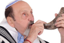 Eldery jewish man blowing the Shofar horn for the Jewish New Year holiday (Rosh Hashanah). Religion concept. Isolated white background