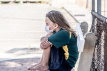 Covid-19 outbreak schools closures. Sad and bored Schoolgirl kid with face mask feeling depressed and lonely outside her closed school. Restrictions and lockdown as Coronavirus containment measures.