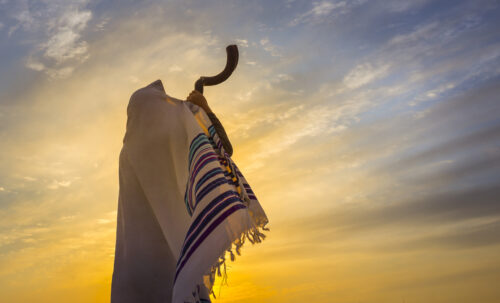 Man in a tallit, Jewish prayer shawl is blowing the shofar ram's horn