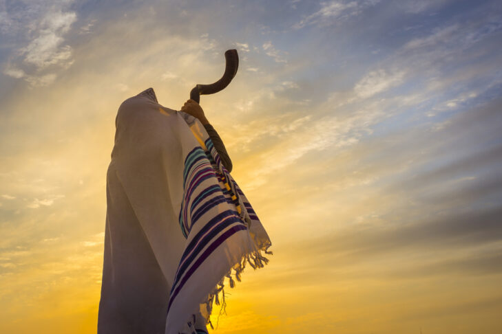 Man in a tallit, Jewish prayer shawl is blowing the shofar ram's horn