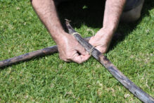 Tying wooden poles to build a sukkah for Sukkot Close up of man hands tying a knot on two pieces of wooden poles on a green grass.