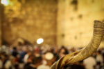 Shofar and in the background, religious people pray at the Western Wall.