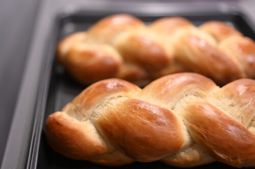 Close up of two cooked challah sweet bread on a baking tray.