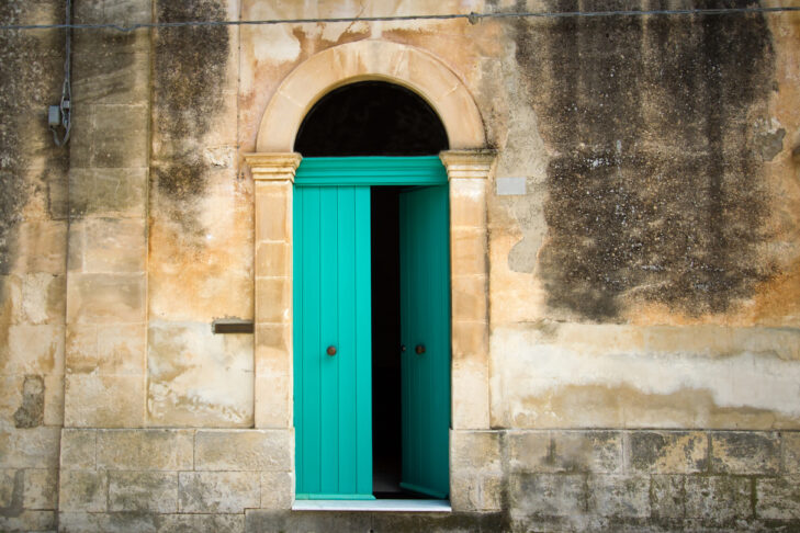 Italian house: a vibrant arched green door (ajar) in a mottled yellow house. Shot in Sicily.