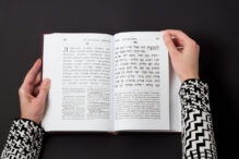 Jewish book, with woman's hand, on black background. Text of the Hebrew, prayer. Woman reading book