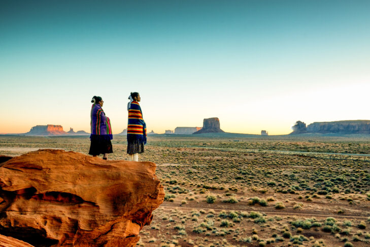 Pretty Navajo girls wrapped in handwoven traditional blankets enjoying a grand sunrise or sunset in Monument Valley