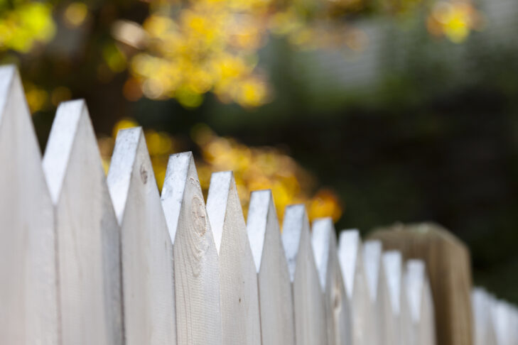 A white picket fence with short focus and an autumn background.