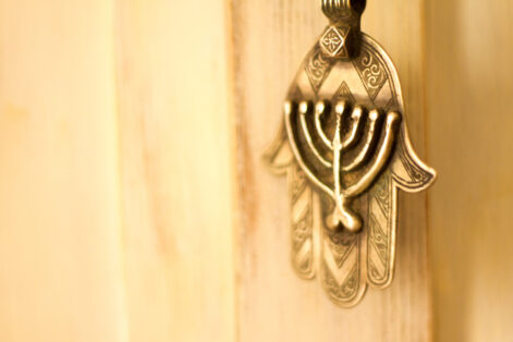 An antique (19th C) ornate silver Khamsa talisman pendant with Jewish menorah design hanging against a pale yellow background. Originally from the Sephardic community in North Africa. Plenty of copy space.