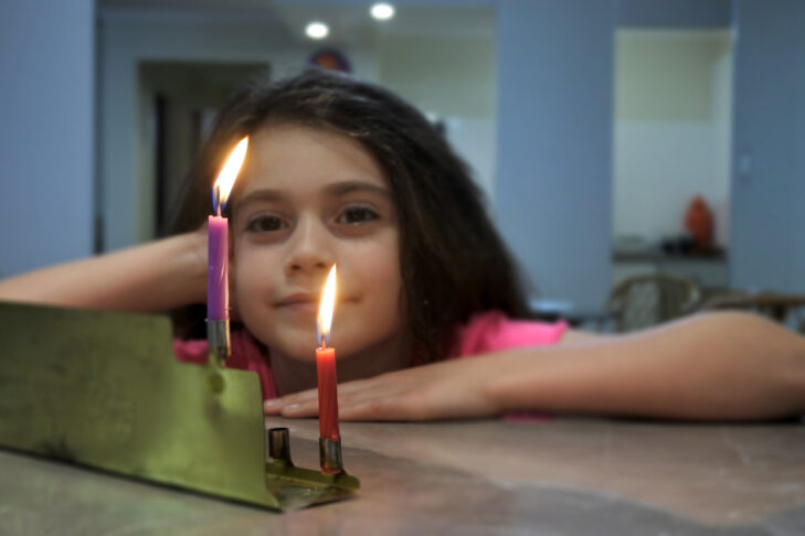 Happy girl looking at the first candles of Chanukah Jewish Holiday on a Chanukiah
