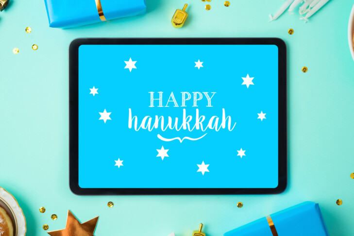 Jewish holiday Hanukkah concept with digital tablet mock up, menorah, sufganiyah and gift box over blue background