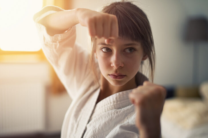 Closeup portrait of little girl aged 10 practicing karate in her room. The girl is lit by sunlight from the window.