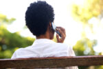 Rear portrait of young woman sitting on a park bench and talking on mobile phone