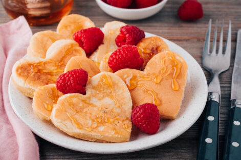 Heart shaped pancakes with raspberries and honey for St. Valentine's Day on wooden baclground