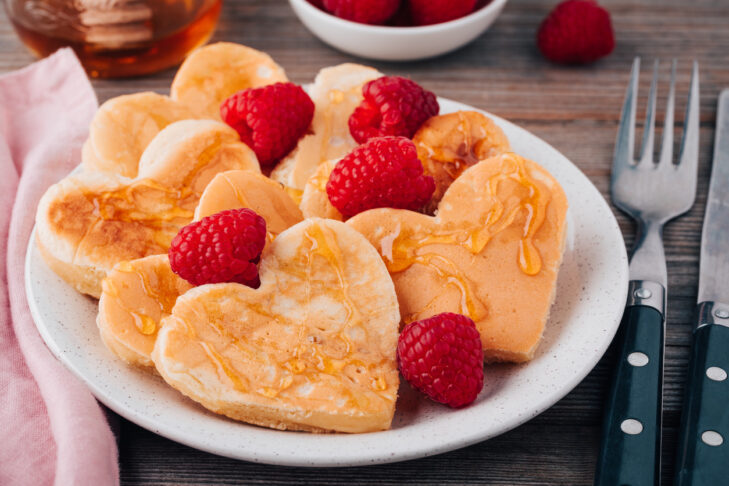 Heart shaped pancakes with raspberries and honey for St. Valentine's Day on wooden baclground