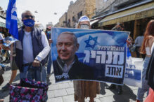 Supporters of Israel's Likud party lift a banner depicting Prime Minister Benjamin Netanyahu during the elections campaign at Mahane Yehuda market in Jerusalem, on March 19, 2021. - Candidates hit the streets ahead of March 23's Israeli election as a world-beating coronavirus vaccination campaign enables face-to-face voter contact, with Prime Minister Benjamin Netanyahu hoping the inoculation effort earns him an elusive majority. (Photo by Emmanuel DUNAND / AFP) (Photo by EMMANUEL DUNAND/AFP via Getty Images)