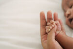 african american new born baby hand holding mom finger on white bed