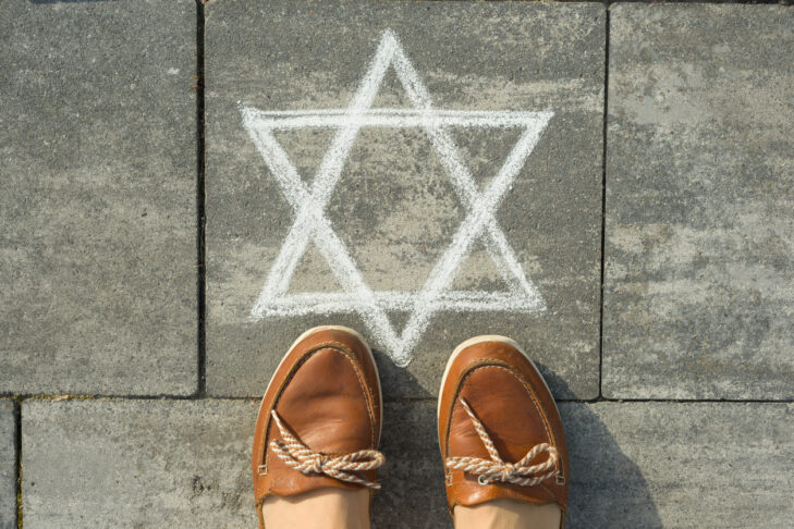 Female feet with abstract image of six pointed star, written on grey sidewalk.