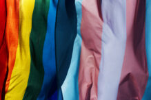 closeup of a gay pride flag and a transgender pride flag waving on the blue sky, moved by the wind