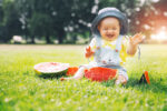Cutest smiling baby girl eating watermelon on green grass in summertime. Funny happy little kid eats healthy fruit snack on nature. Image of Childhood, Family, Baby Feeding.