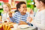 Colorful portrait of multi-ethnic group of children eating pizza enjoying awesome  party in cafe, focus on African-American boy laughing happily