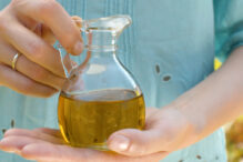 Close up olive oil in female hands in a glass jug in the garden at summer day. Healthy lifestyle concept