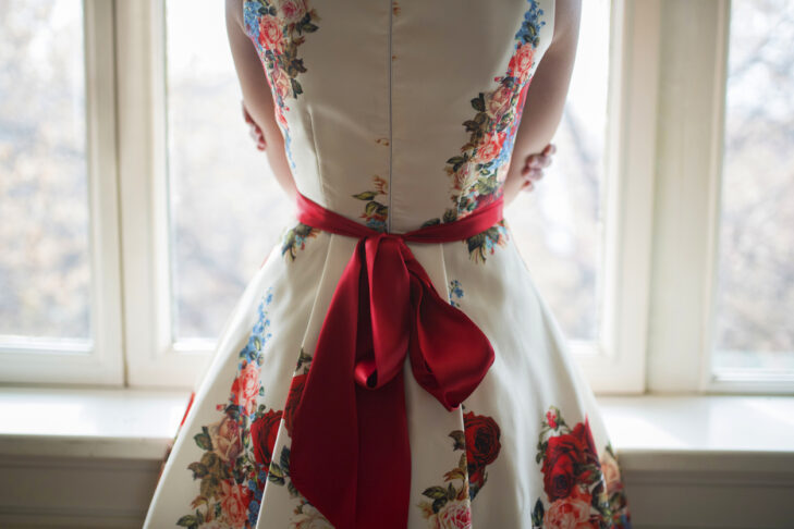 Unrecognizable female in a floral dress. Focus on red belt tied in a bow.