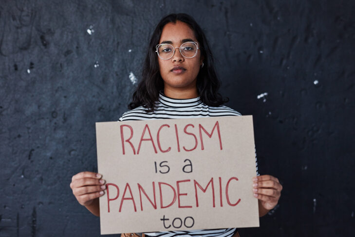 Studio shot of a young woman protesting against racism against a dark background
