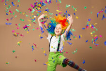 Little boy in clown wig jumping and having fun celebrating birthday. Portrait of a child throws up a multi-colored tinsel and confetti. Birthday boy. Positive emotions.