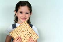 Cute Jewish girl (age 06) looking at camera  holding Matzo bread on Passover Jewish holiday. Real people. Copy space