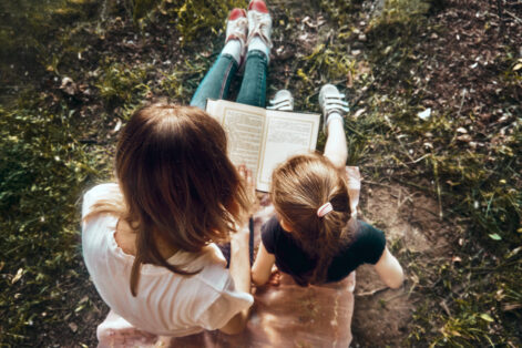 Mom and daughter on a sunny summer day in the park read a book. A place to relax, a time of mother and daughter. Fresh air in nature.