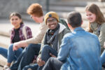 A multi ethnic group of university students are hanging out outdoors on campus.