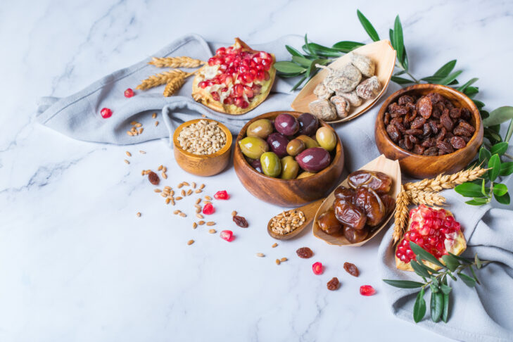 Symbols of judaic holiday Tu Bishvat, Rosh Hashana new year of the trees. Mix of dried fruits, date, fig, grape, barley, wheat, olive, pomegranate on a wooden table. Copy space background