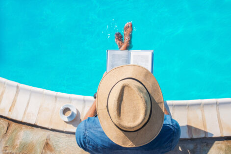 photo of a man reading a book next to the swimming pool,relaxing,sitting on the edge with his legs in the water