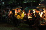 Slichot Services with people seated in the garden holding candles and umbrellas
