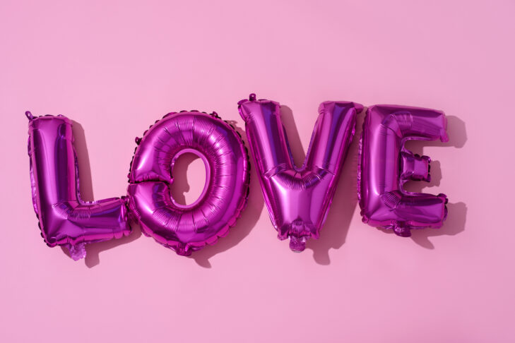some fuchsia letter-shaped balloons forming the word love against a pink background