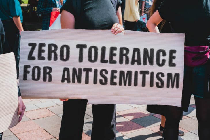 The phrase " Zero tolerance for antisemitism " drawn on a carton banner in hand. A girl holds a cardboard with an inscription. Girls on the street. Protest, march. Rally.