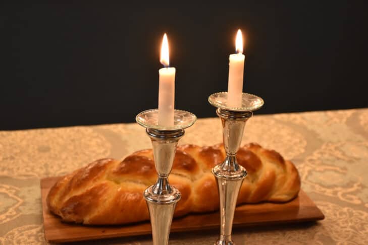 Two lit Shabbat candles in front of challah
