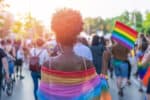 Rear view image of young African-American woman walking at the LGBTQI pride event and waving rainbow flag