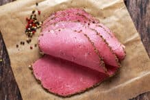 Peppered roast beef pastrami slices on paper with grains of coloured pepper