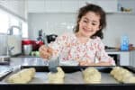 Happy young Jewish girl (female age 7) baking sweet Challah bread for Sabbath Jewish Holiday in home kitchen.