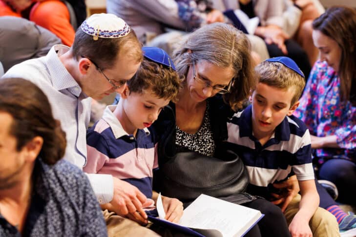 Two young boys and their parents looking at a prayerbook during High Holy Day services