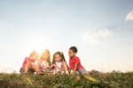 Group of little children reading children's book while relaxing in grass at sunset. Copy space.