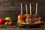 Autumn candy apples with chocolate and caramel, side view on a rustic wood platter