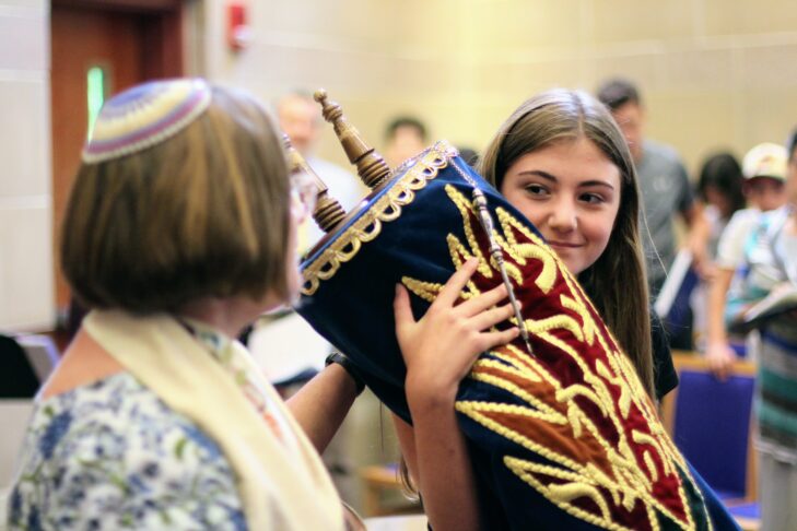 A young girl holding a Torah with a female Rabbi next to her