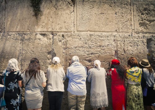 Jerusalem, Israel - August 2018: Women praying at the Western Wall, which is one of Judaism most holy places and located in the old city of Jerusalem. The wall is cracked and in the cracks are pieces of paper with prayer notes.