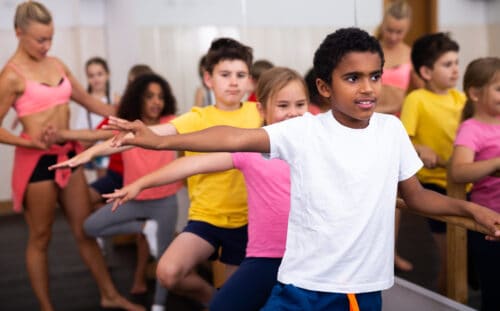 Smiling african boy practicing classic dance moves near ballet barre during group class